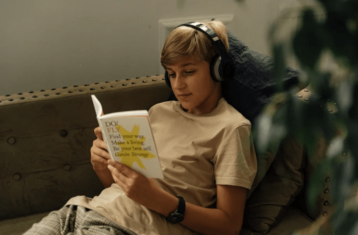 Gambar seseorang belajar Bahasa Inggris dengan laptop dan headphone di kafe.